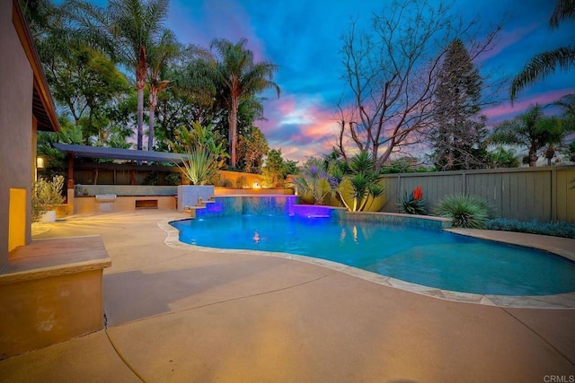 pool at dusk featuring a fenced in pool, an outdoor kitchen, a fenced backyard, and a patio area