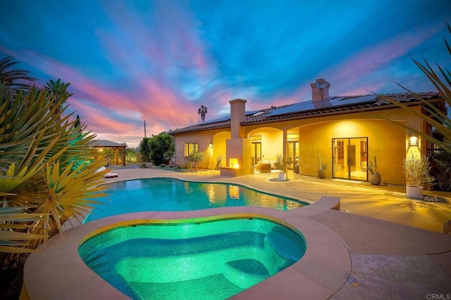 pool at dusk with an outdoor pool, a patio, and an in ground hot tub