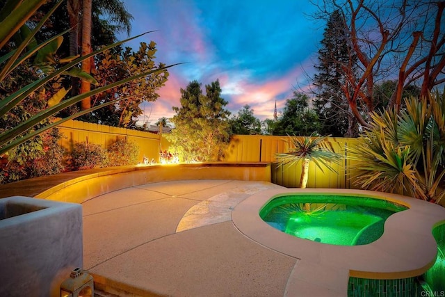 pool at dusk with a patio area and a fenced backyard