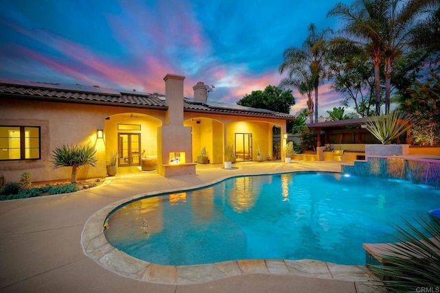 pool at dusk with a patio, french doors, and an outdoor pool