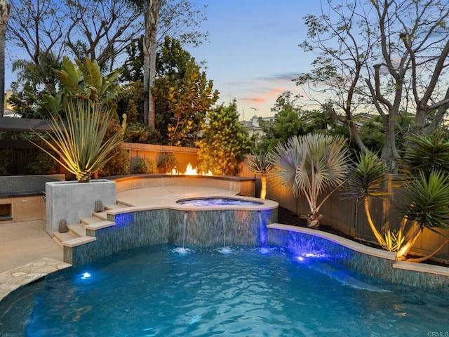 pool at dusk with a patio, an in ground hot tub, a fenced in pool, and a fenced backyard