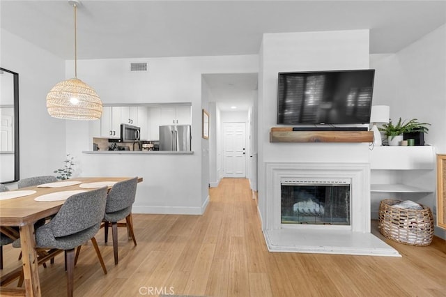 dining area featuring light wood-type flooring, visible vents, baseboards, and a glass covered fireplace