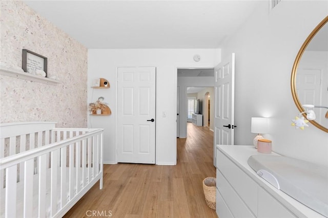 bedroom featuring light wood finished floors, a crib, and baseboards