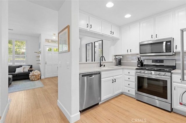 kitchen featuring a sink, white cabinetry, appliances with stainless steel finishes, light wood finished floors, and light countertops