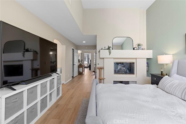 bedroom featuring baseboards, a multi sided fireplace, and light wood-style floors