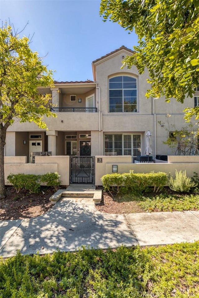 view of front of property featuring a fenced front yard, stucco siding, a balcony, and a gate