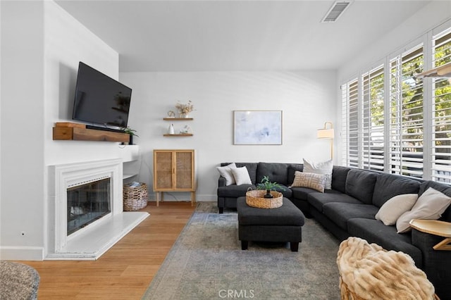 living area with visible vents, baseboards, a glass covered fireplace, and wood finished floors