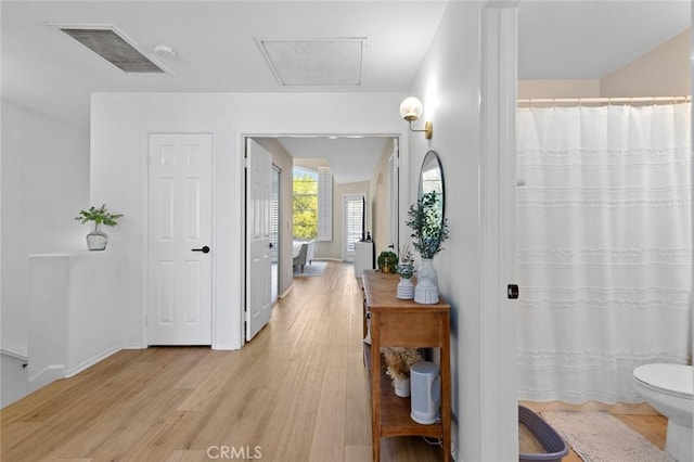 hall featuring visible vents, baseboards, and light wood finished floors