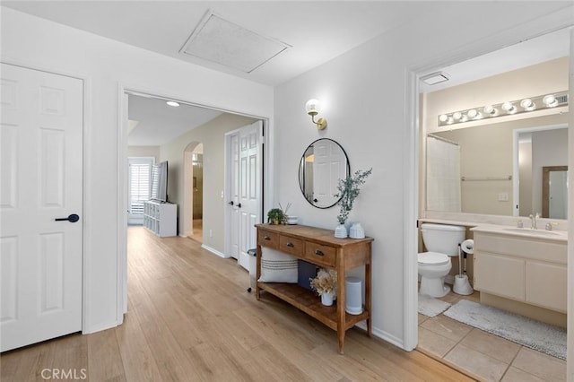 corridor with a sink, baseboards, arched walkways, and light wood-style flooring