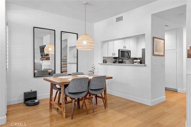 dining space featuring stairs, light wood-style flooring, baseboards, and visible vents