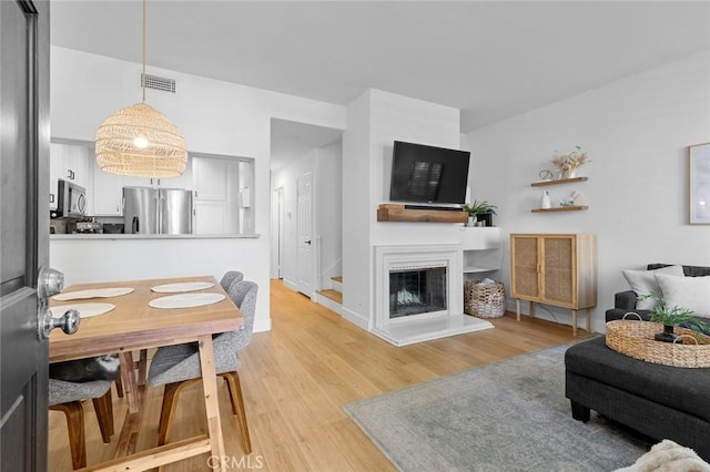 living area with light wood finished floors, visible vents, baseboards, stairway, and a glass covered fireplace