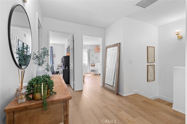 corridor featuring baseboards, visible vents, and light wood finished floors