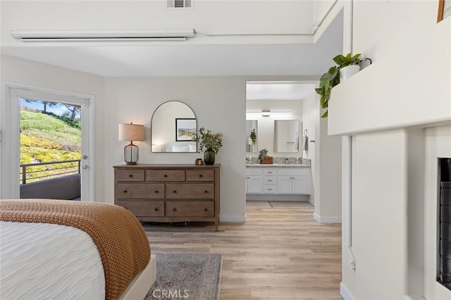 bedroom featuring baseboards, light wood finished floors, ensuite bath, a sink, and access to exterior