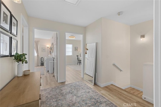 corridor featuring an upstairs landing, washing machine and dryer, light wood-type flooring, and baseboards