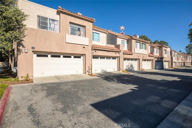 view of front of property featuring stucco siding, a residential view, a garage, and a tiled roof