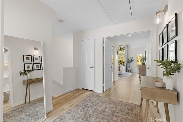 corridor with baseboards, attic access, and light wood-style flooring