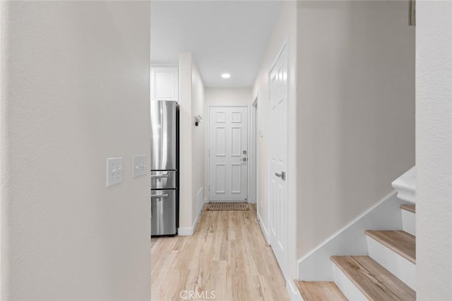 corridor with light wood finished floors, stairs, and baseboards