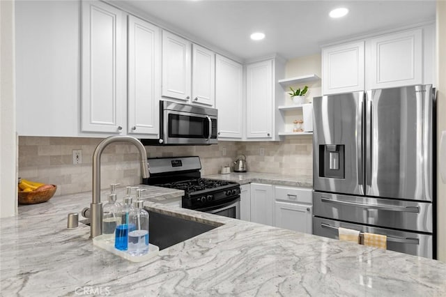 kitchen with light stone countertops, open shelves, white cabinets, appliances with stainless steel finishes, and tasteful backsplash