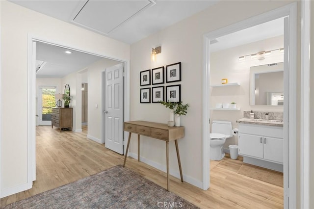 corridor with light wood-style flooring, baseboards, and a sink