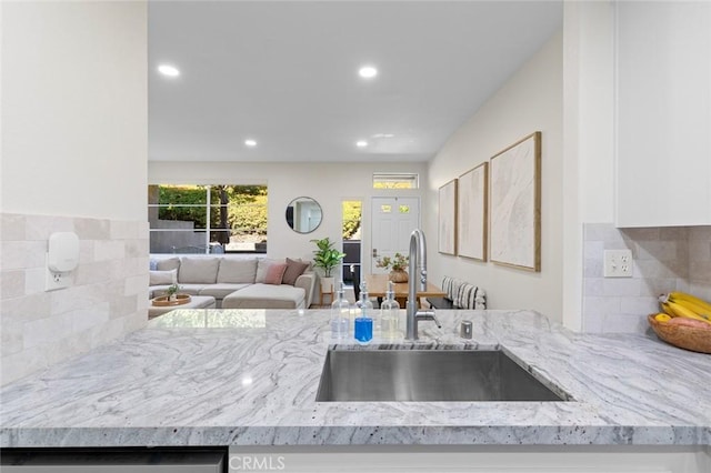 kitchen featuring a sink, light stone counters, tasteful backsplash, open floor plan, and recessed lighting