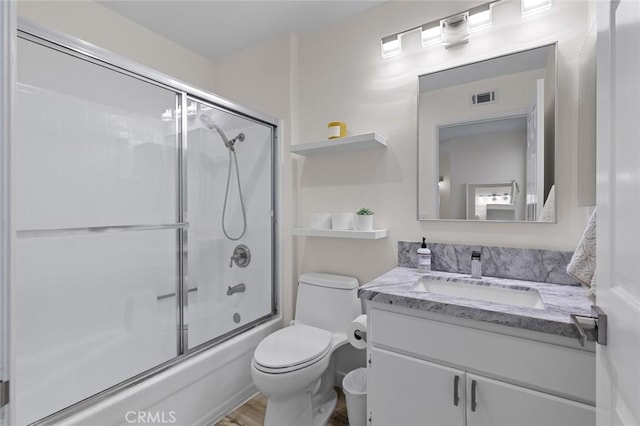 bathroom with visible vents, toilet, wood finished floors, shower / bath combination with glass door, and vanity