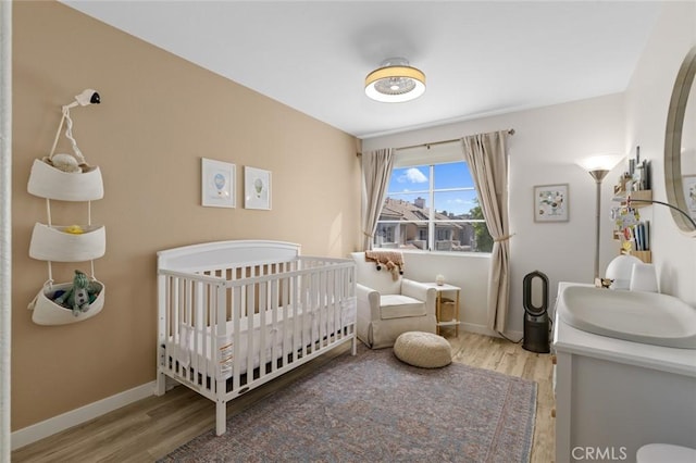 bedroom featuring baseboards, a nursery area, and wood finished floors