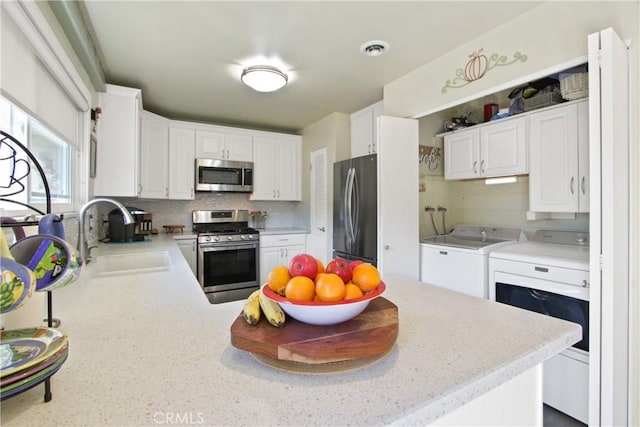 kitchen featuring visible vents, washing machine and clothes dryer, a sink, stainless steel appliances, and tasteful backsplash