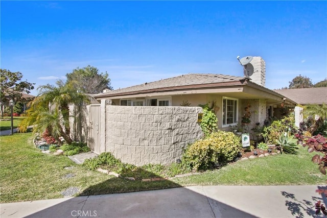 view of side of property featuring a tile roof, fence, a lawn, and stucco siding