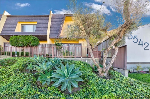 townhome / multi-family property featuring mansard roof and fence