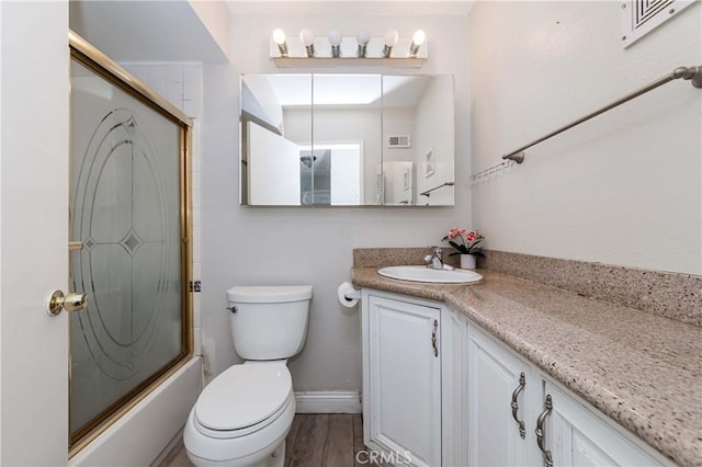 bathroom with toilet, wood finished floors, baseboards, bath / shower combo with glass door, and vanity