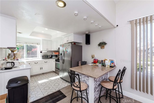 kitchen with appliances with stainless steel finishes, a peninsula, a kitchen breakfast bar, white cabinetry, and a raised ceiling