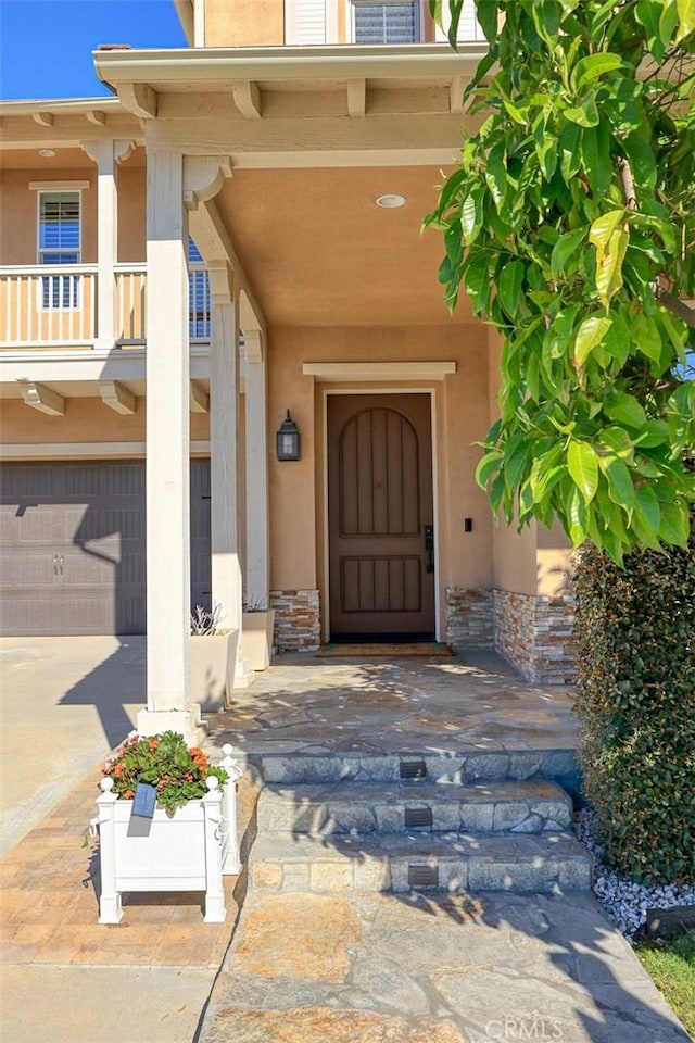 property entrance featuring stucco siding, an attached garage, and a balcony