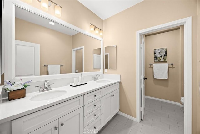 bathroom with double vanity, toilet, baseboards, and a sink