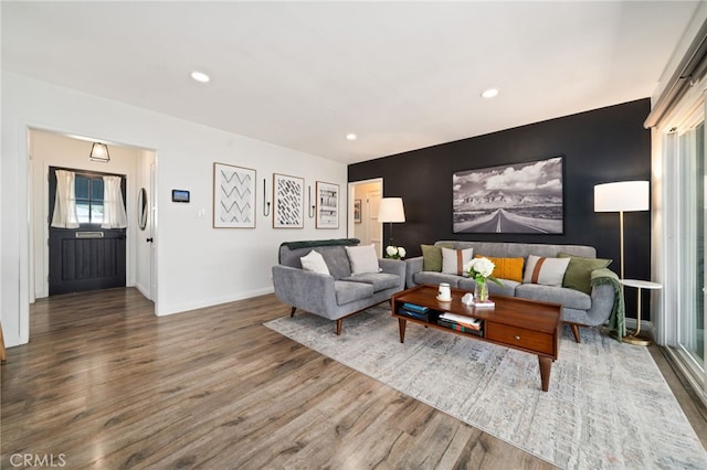 living room with an accent wall, recessed lighting, wood finished floors, and baseboards