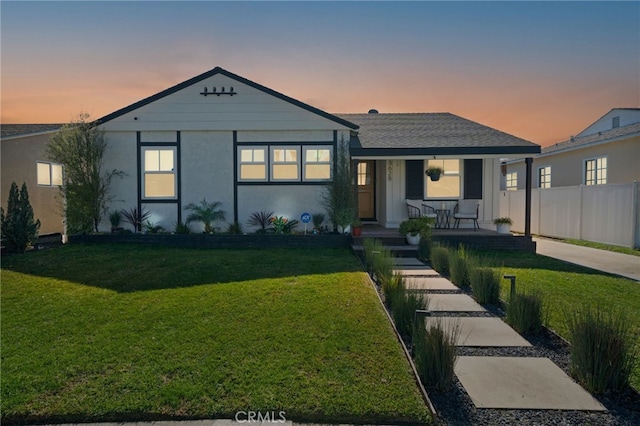 view of front of house with stucco siding, a porch, a yard, and fence