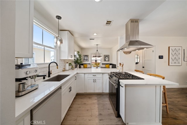 kitchen featuring gas stove, a peninsula, island exhaust hood, a sink, and backsplash