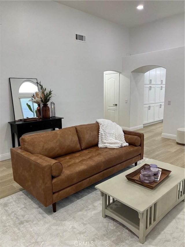 living room featuring arched walkways, visible vents, light wood finished floors, and baseboards