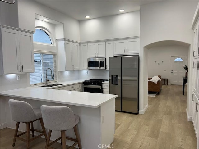 kitchen featuring arched walkways, a peninsula, stainless steel appliances, and a towering ceiling