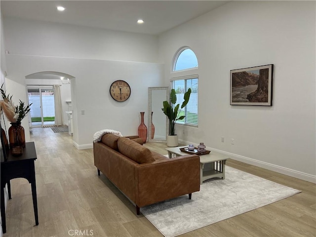 living room with baseboards, arched walkways, a high ceiling, and light wood finished floors