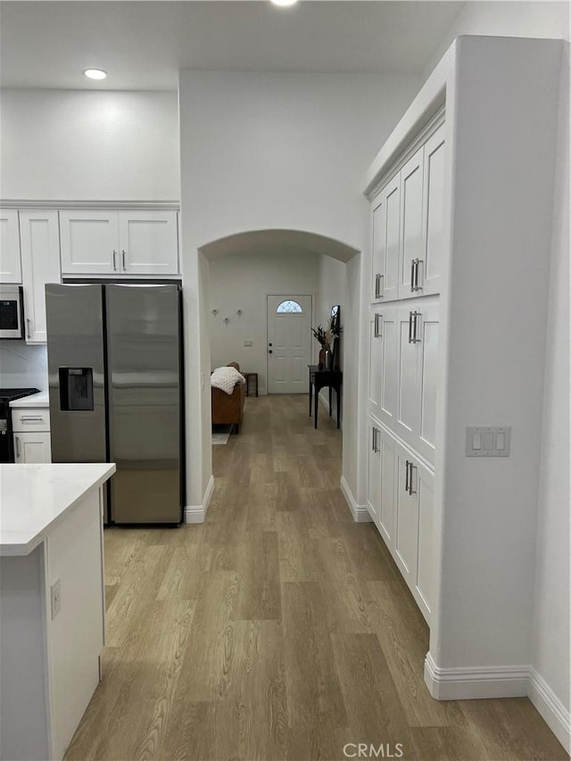 kitchen with light wood finished floors, light countertops, white cabinets, arched walkways, and stainless steel fridge