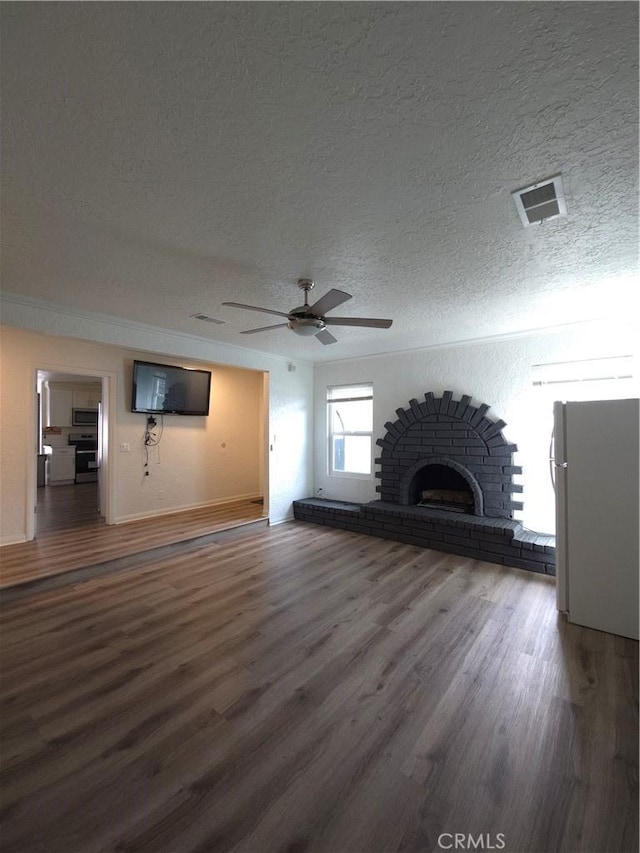 unfurnished living room featuring visible vents, a ceiling fan, a textured ceiling, wood finished floors, and a brick fireplace