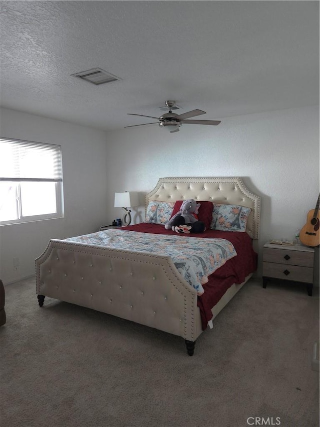 bedroom featuring light carpet, visible vents, a textured ceiling, and ceiling fan