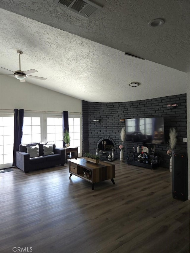 living room with wood finished floors, visible vents, vaulted ceiling, a textured ceiling, and a brick fireplace