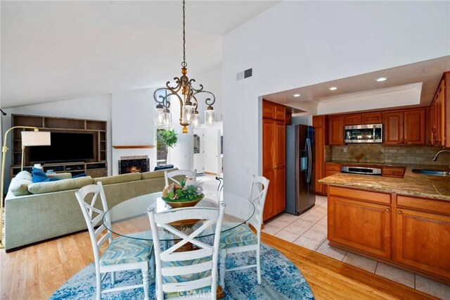 dining area featuring light wood finished floors, visible vents, a warm lit fireplace, and an inviting chandelier