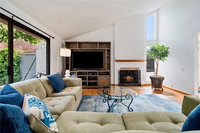 living room featuring vaulted ceiling, baseboards, a fireplace with flush hearth, and wood finished floors