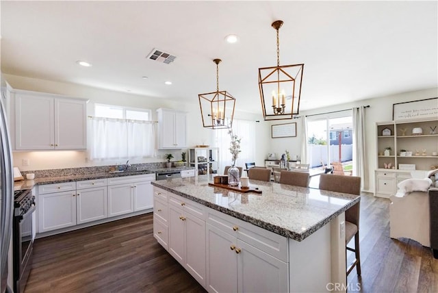 kitchen with dark wood-style floors, visible vents, stainless steel appliances, white cabinets, and a kitchen bar