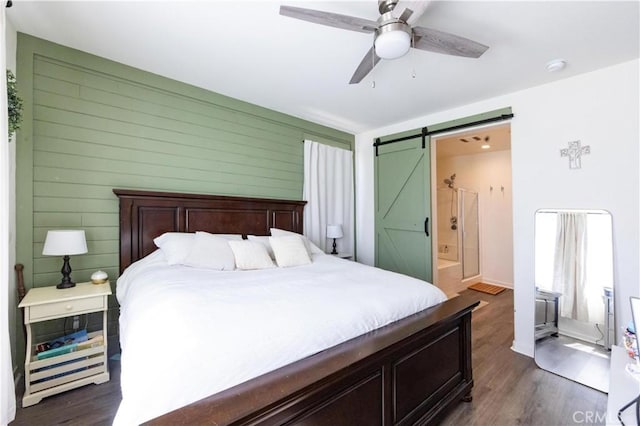 bedroom with connected bathroom, ceiling fan, wood walls, a barn door, and dark wood-style floors