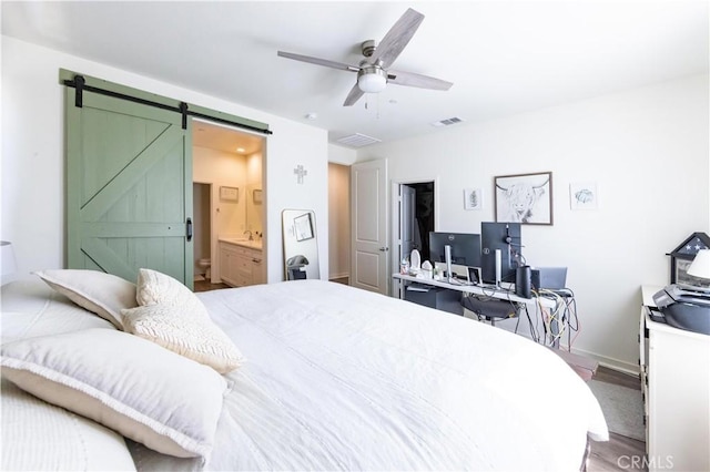 bedroom featuring wood finished floors, visible vents, ensuite bath, ceiling fan, and a barn door