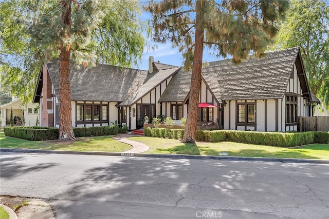 tudor-style house with stucco siding, a chimney, and a front lawn