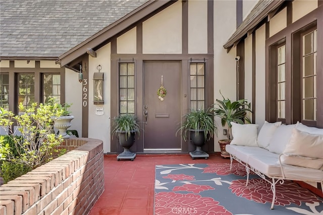 doorway to property featuring stucco siding, an outdoor hangout area, and roof with shingles